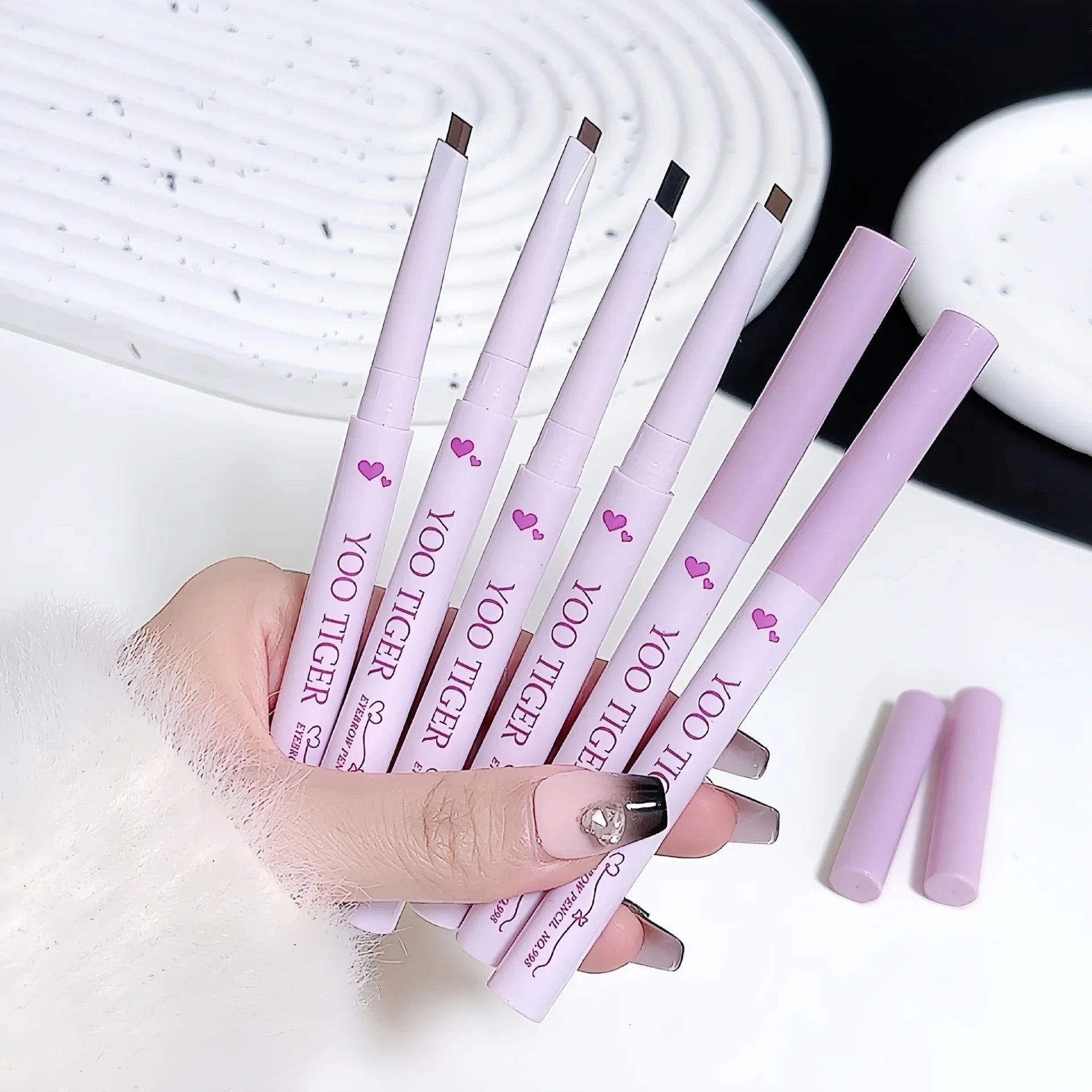 Hand holding multiple YOO TIGER eyebrow pencils in pastel tubes, Omgbeautyessential product